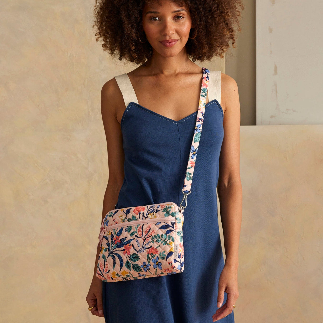 model wearing blue dress with pink crossbody bag that has a multi-color floral pattern