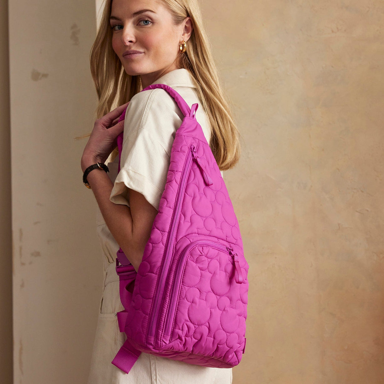 model holding pink sling quilted backpack with mickey mouse pattern