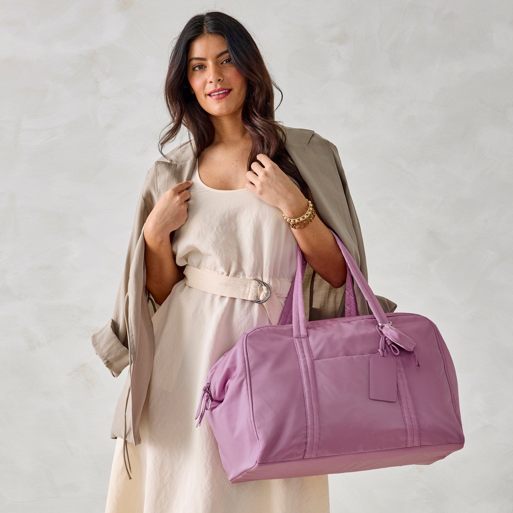 model wearing cream dress and light brown jacket with large purple nylon weekend bag over arm
