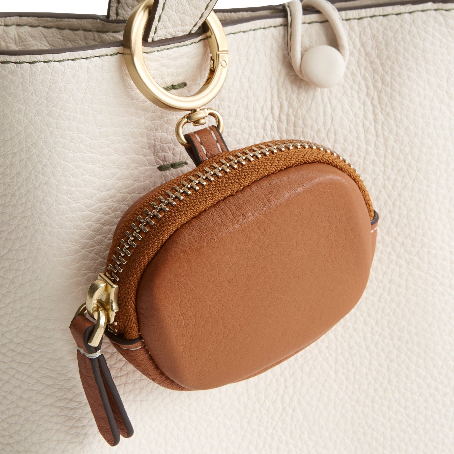 light brown leather bag charm for airpods clipped onto strap of cream leather handbag