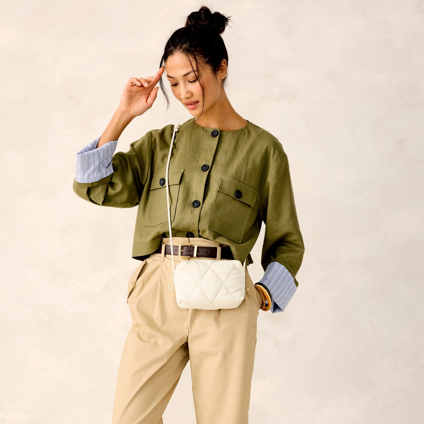 model wearing green shirt with cream colored quilted crossbody bag across shoulder