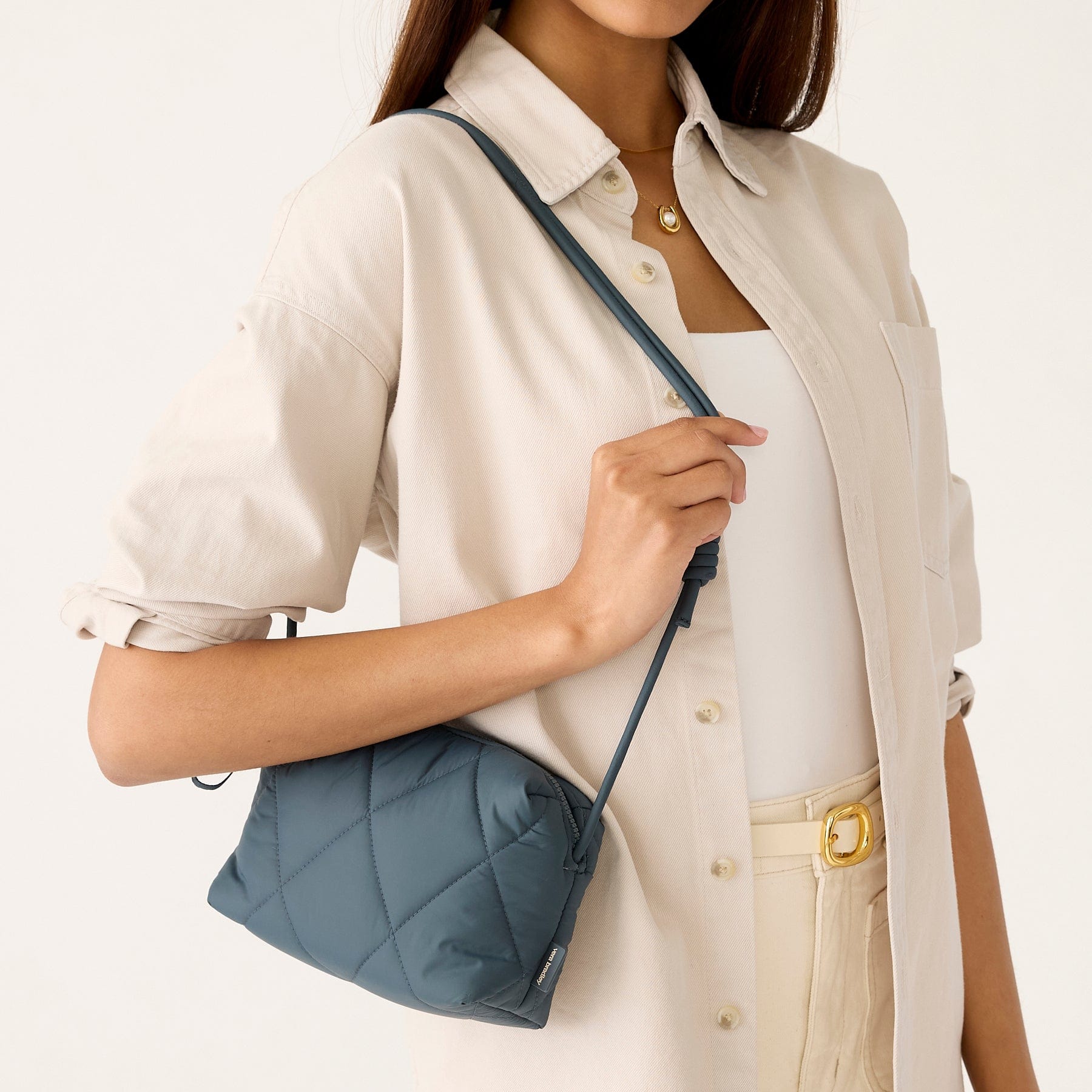 model wearing cream button down shirt with small dark slate blue quilted purse over shoulder