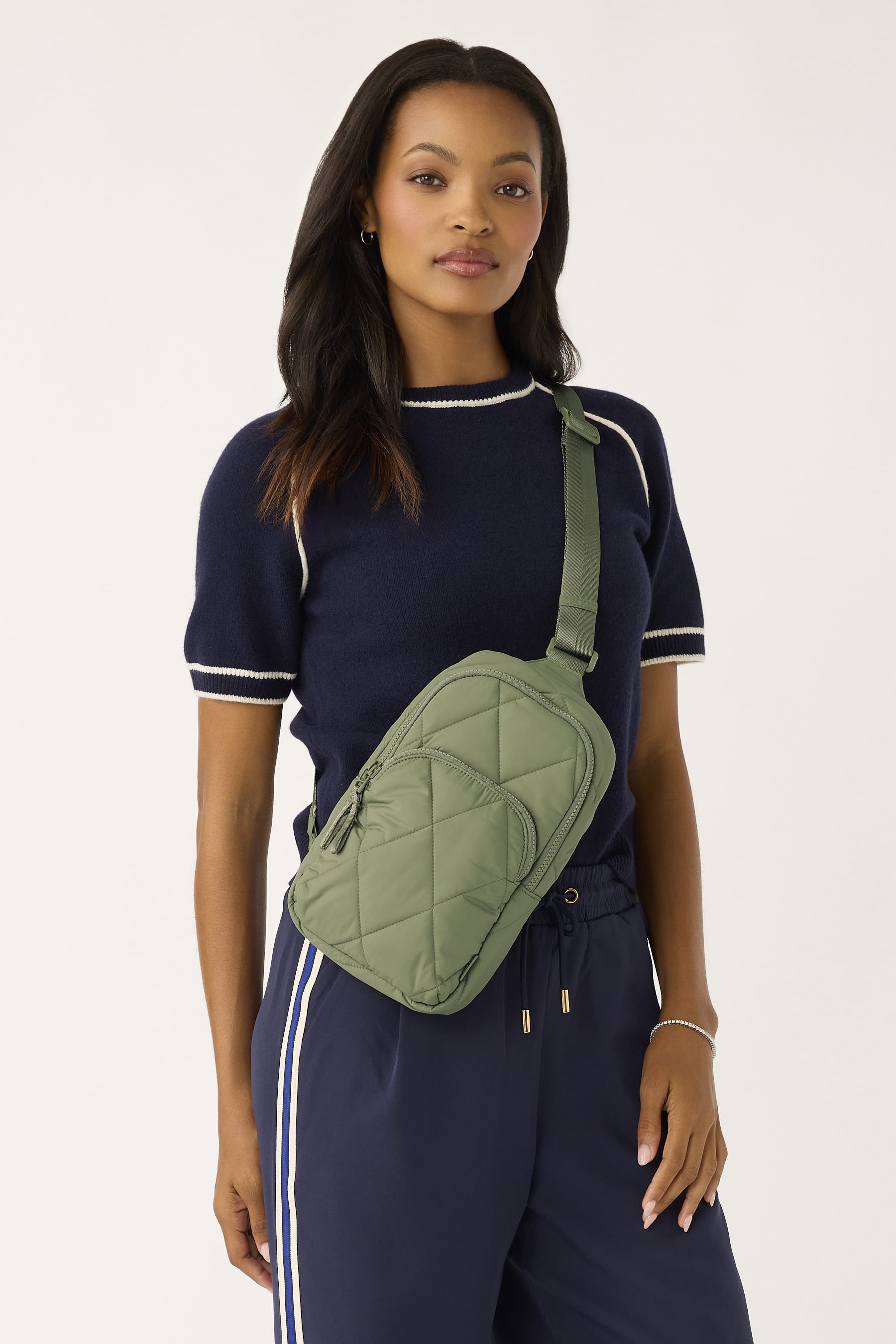 model wearing navy blue casual outfilt with lighweight natural green quilted nylon sling bag slung across chest