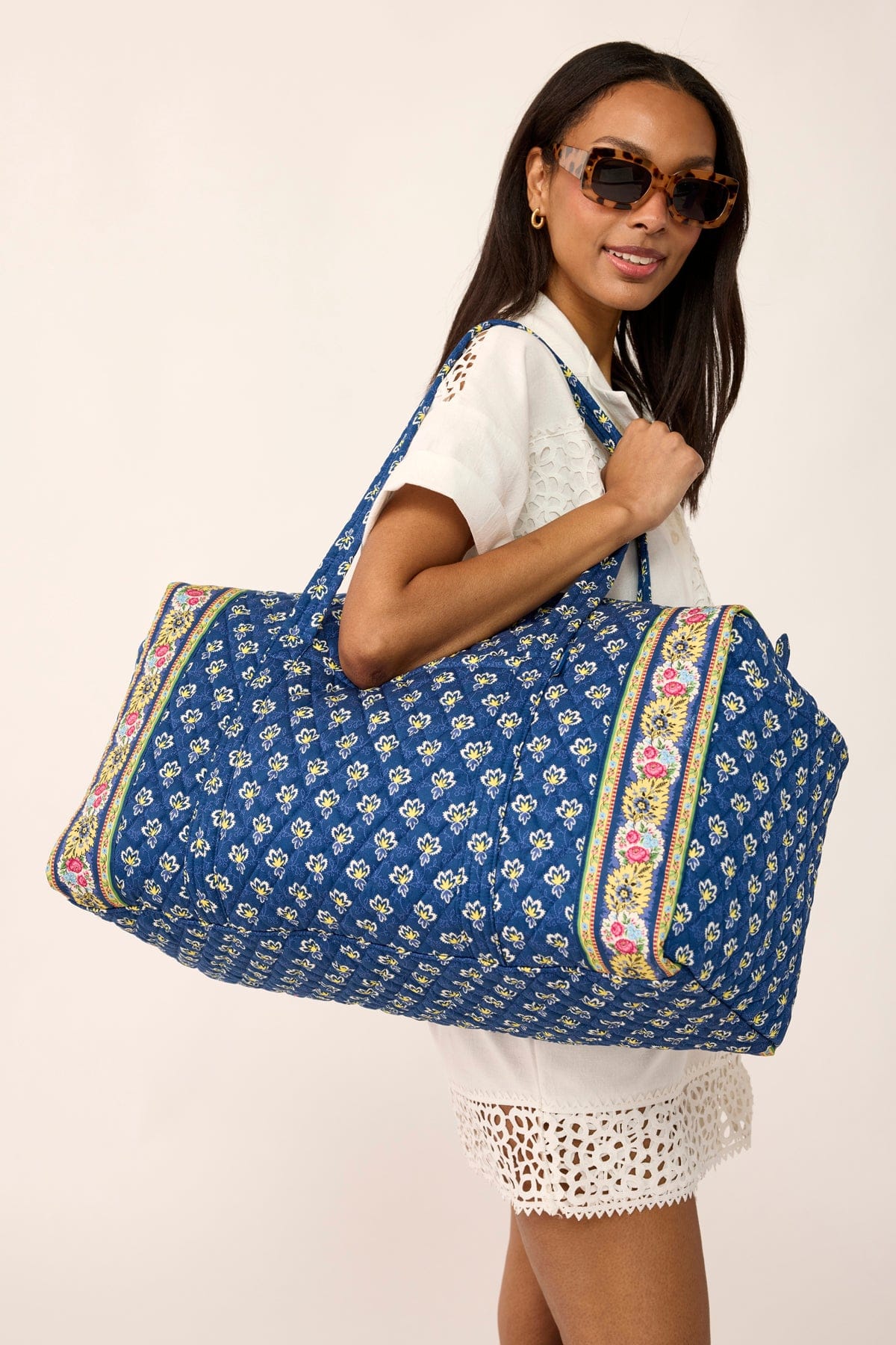 model wearing cream dress and sunglasses with large blue quilted cotton duffel bag over shoulder