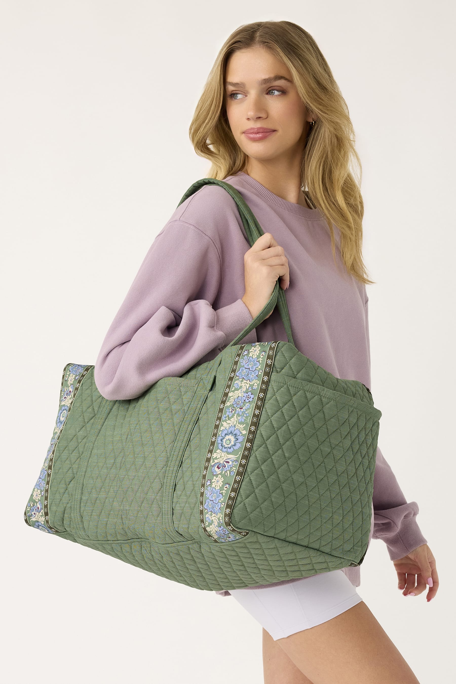 model wearing light purple sweatshirt with large green quilted cotton backpack with floral patterned bands slung over shoulder