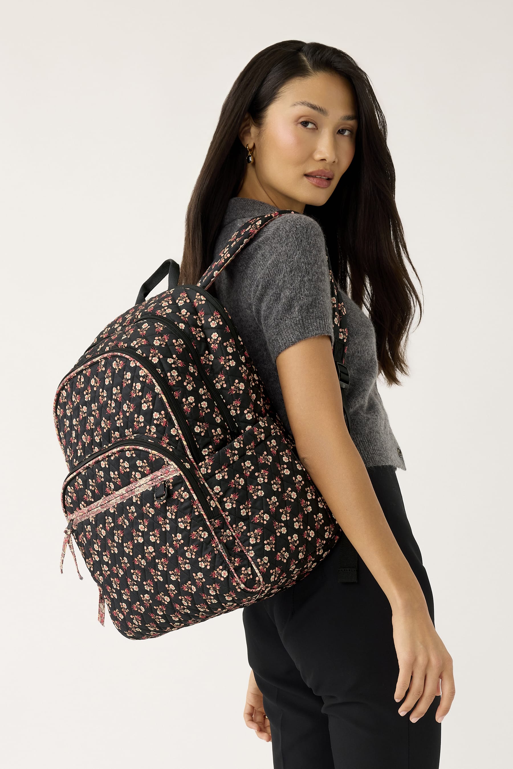 model wearing grey sweater and black pants with black quilted cotton backpack featuring small pink flowers pattern slung over shoulder