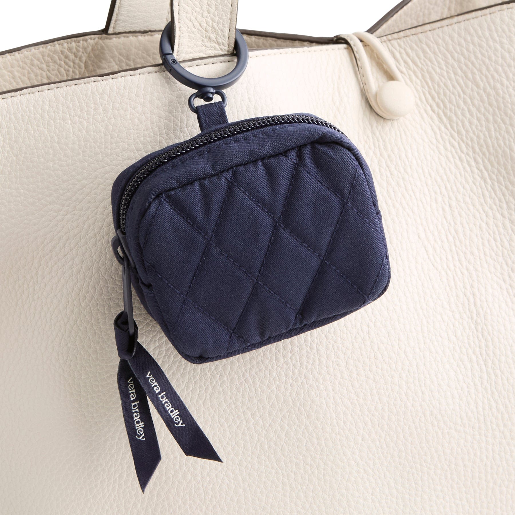navy blue zippered earbud case shown with metal hinge ring around handle on cream leather purse