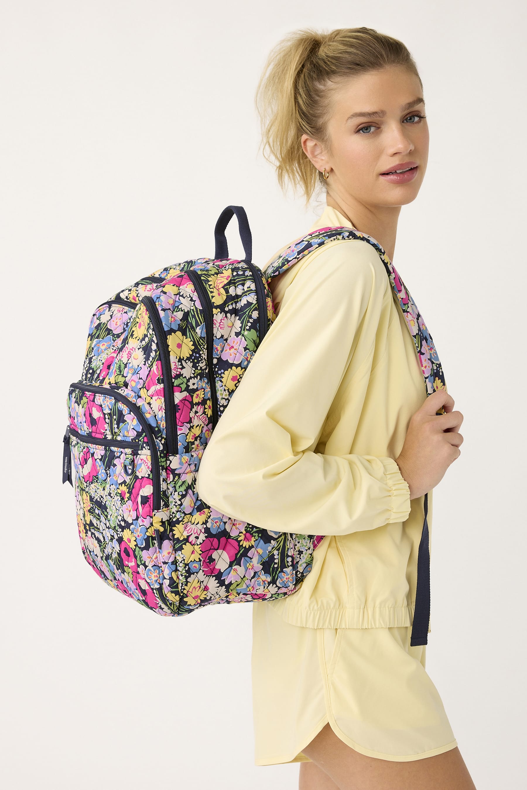 model wearing yellow shirt and shorts with large black quilted cotton backpack featuring bright multicolor wildflowers pattern