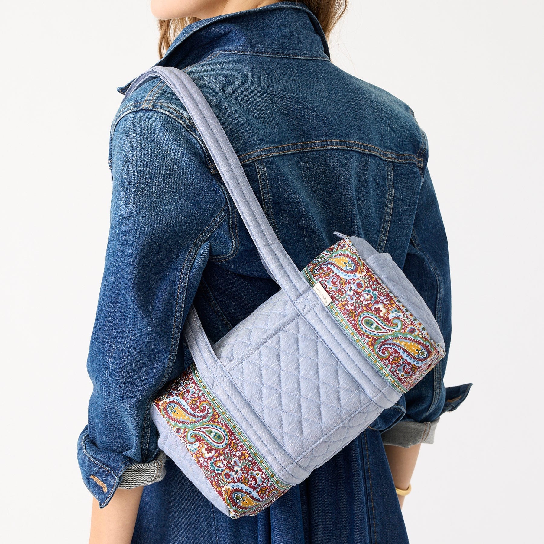 back of model wearing denim with vera bradley original 100 blue chambray quilted cotton handbag with paisley pattern