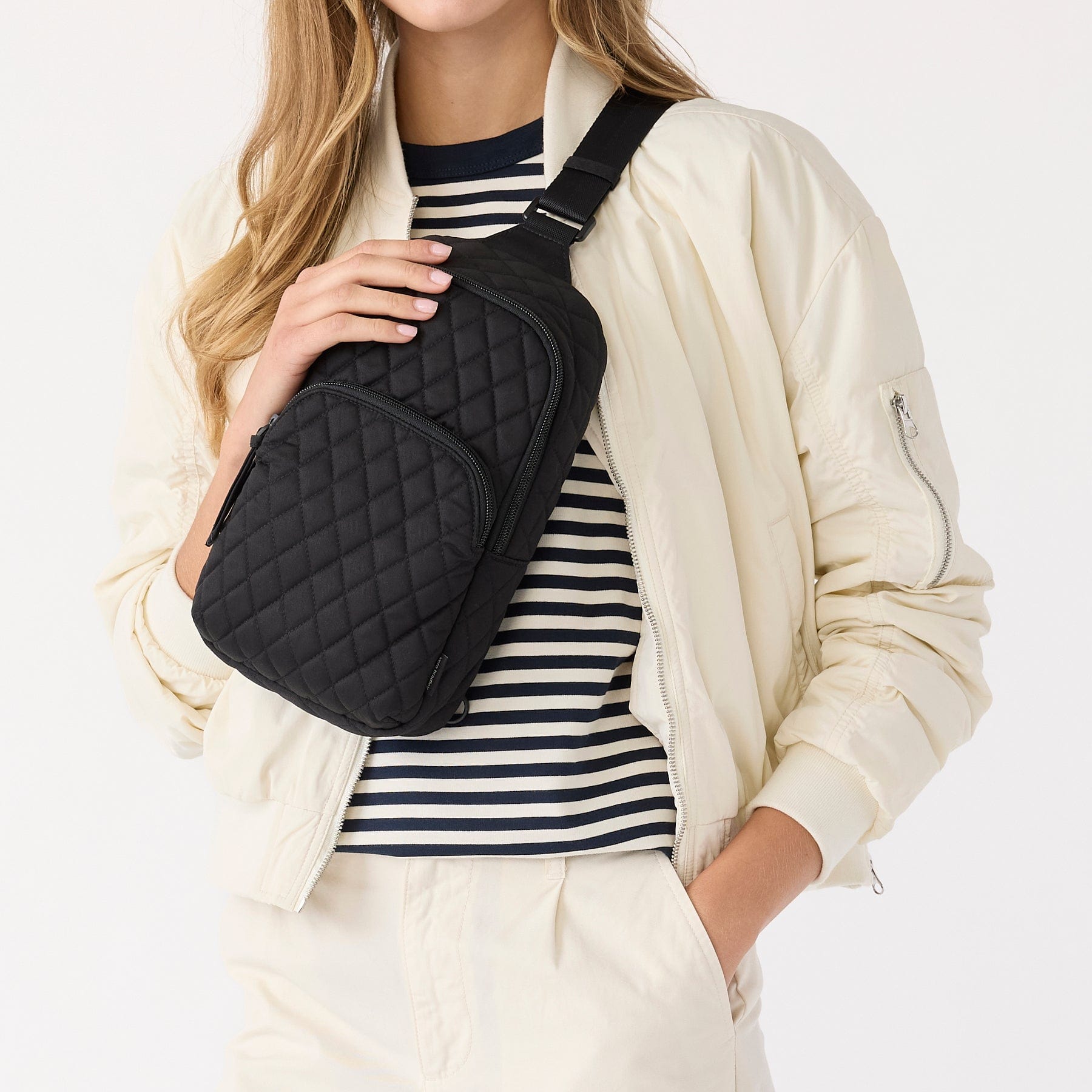 model wearing white jacked over striped shirt with small black quilted cotton sling backpack across chest