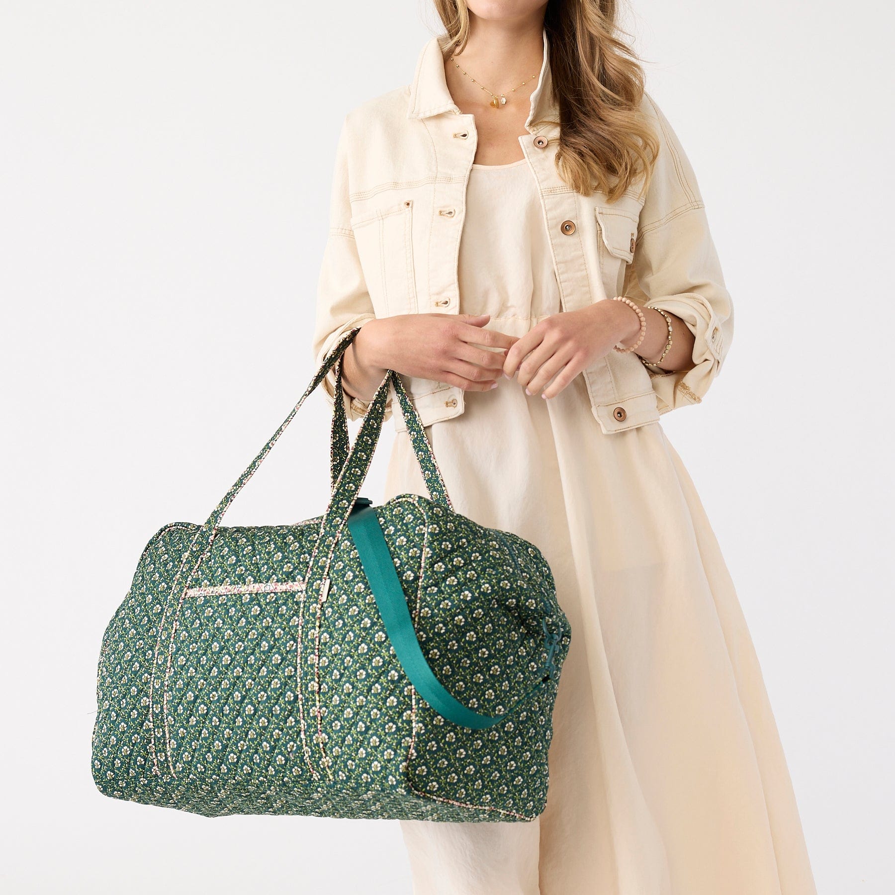 model wearing cream jacket and dress carrying green quilted cotton overnight bag with small white floral pattern