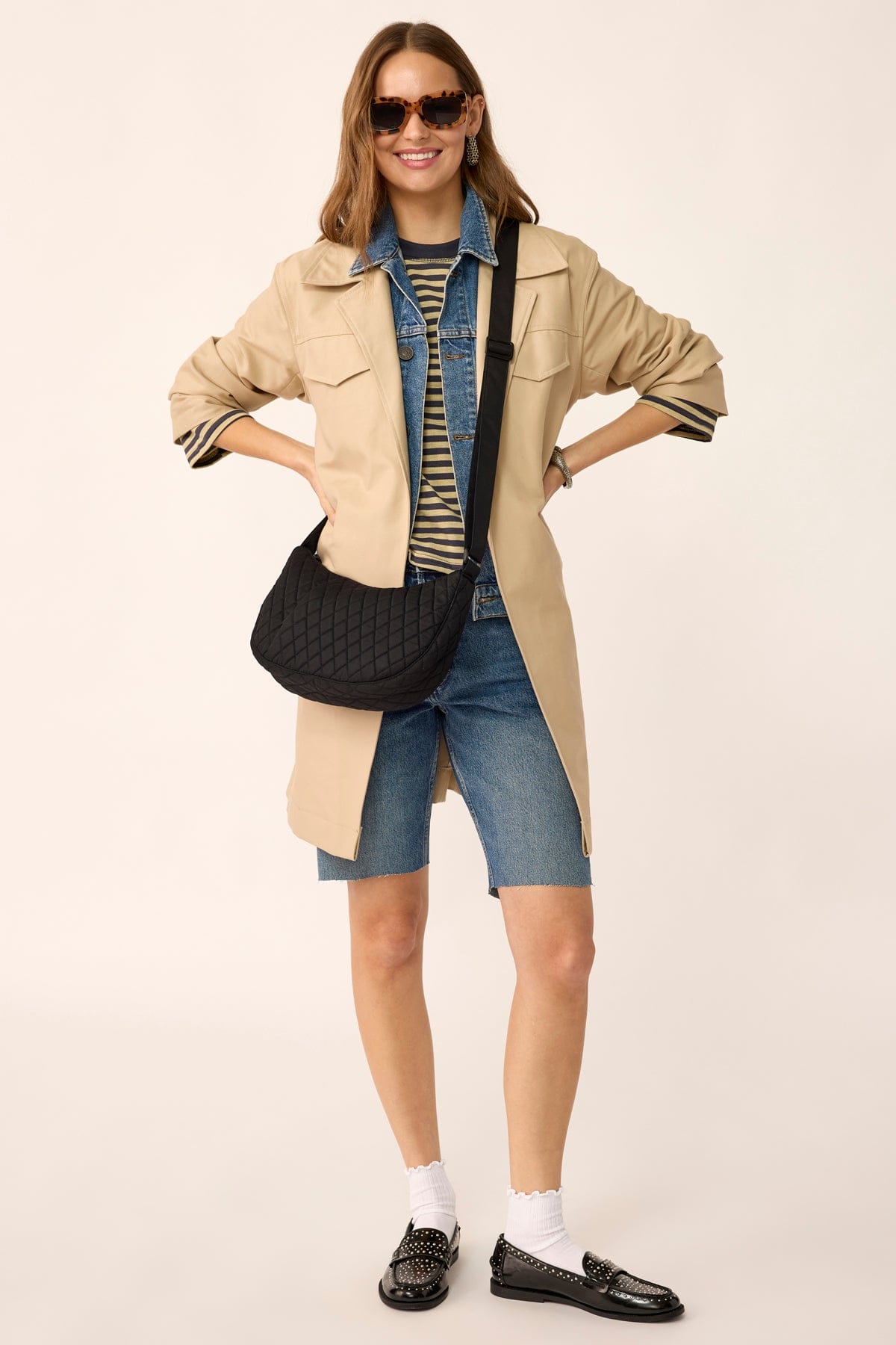 model wearing sunglasses and long brown jacket with small black quilted cotton crossbody bag