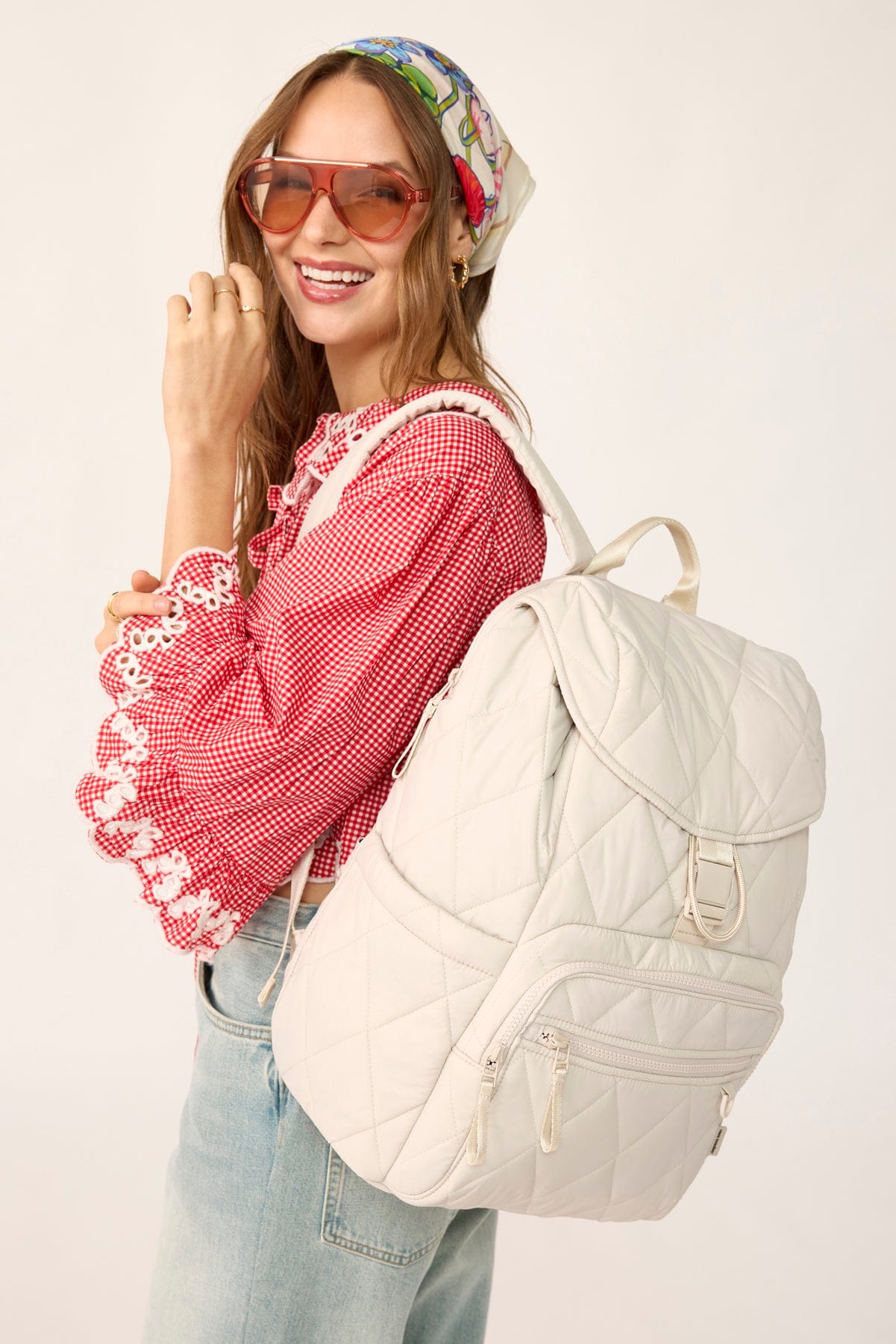 model wearing red checked blouse and light jeans with large cream quilted backpack over shoulder