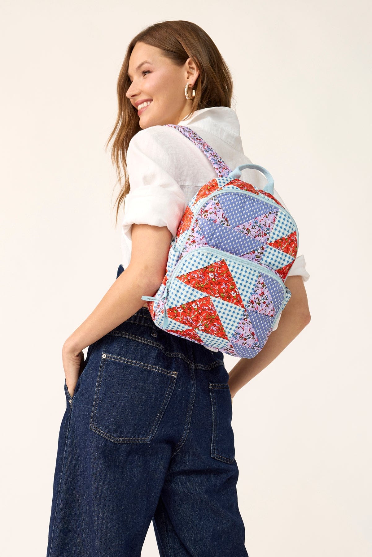 model wearing dark denim jeans white shirt and small cotton backpack with patchwork quilt pattern slung over shoulder
