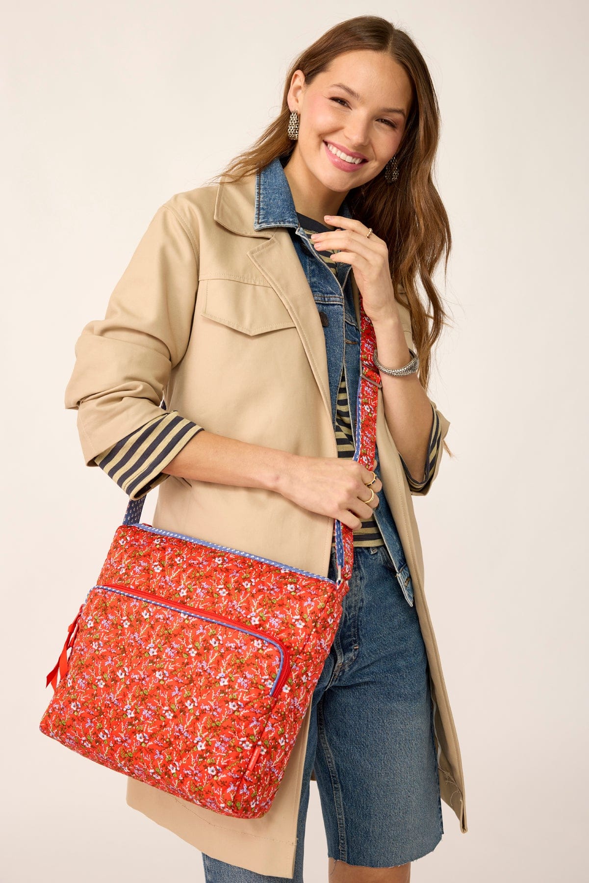 model wearing light tan jacket over denim outfit with large red crossbody bag with small white floral pattern