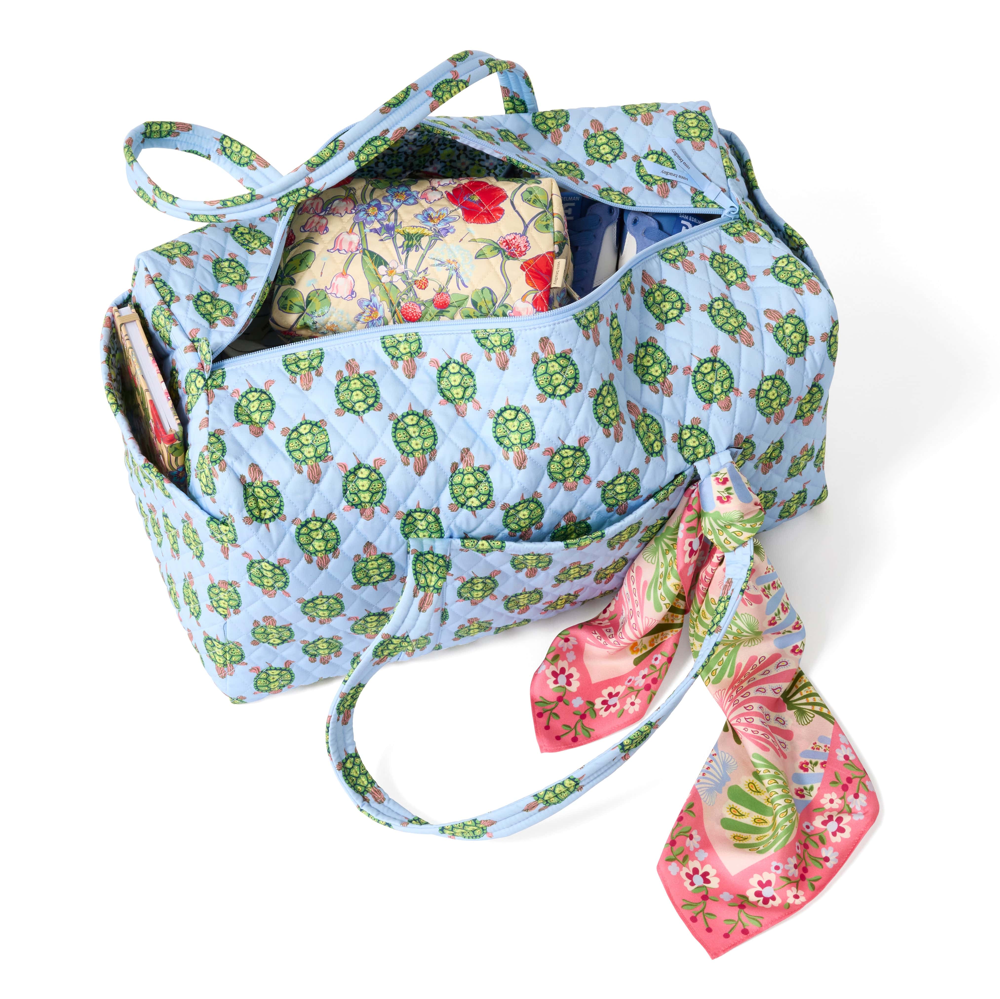 large pale blue quilted cotton duffel bag with turles pattern shown unzipped with floral cosmetic bag inside and book in exterior slip pocket